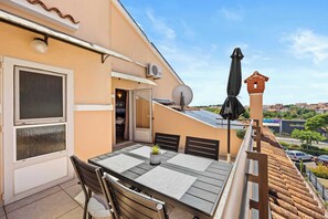 Ein Balkon mit Tisch, Stühlen, einer Topfpflanze und einem schwarzen Sonnenschirm.