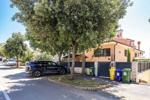 Una calle residencial con una camioneta estacionada, aceras arboladas y una casa con entrada protegida por una reja.
