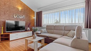 Una sala moderna con un televisor de pantalla plana grande, un sofá color beige, una mesa de centro de madera y un elemento decorativo en la pared.