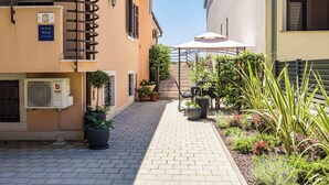 A narrow alleyway with a paved path, potted plants, and a staircase leading to a building entrance.