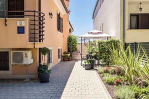 A narrow alleyway with a paved path, potted plants, and a staircase leading to a building entrance.