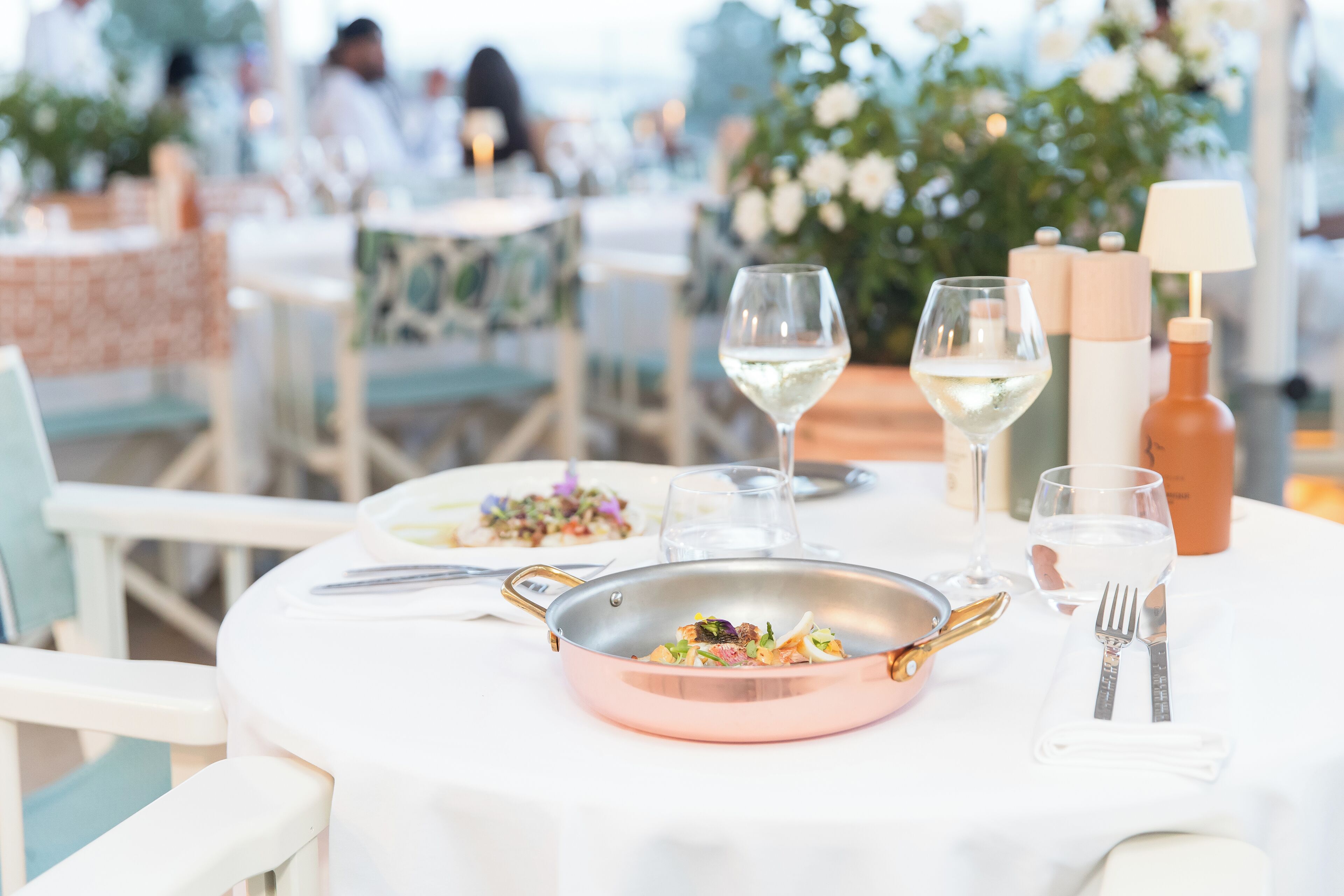 Une table dressée pour le repas, avec une casserole en cuivre, des verres à vin et des couverts.