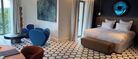 A modern hotel room with a large bed, a round dining table, and a seating area with blue chairs.