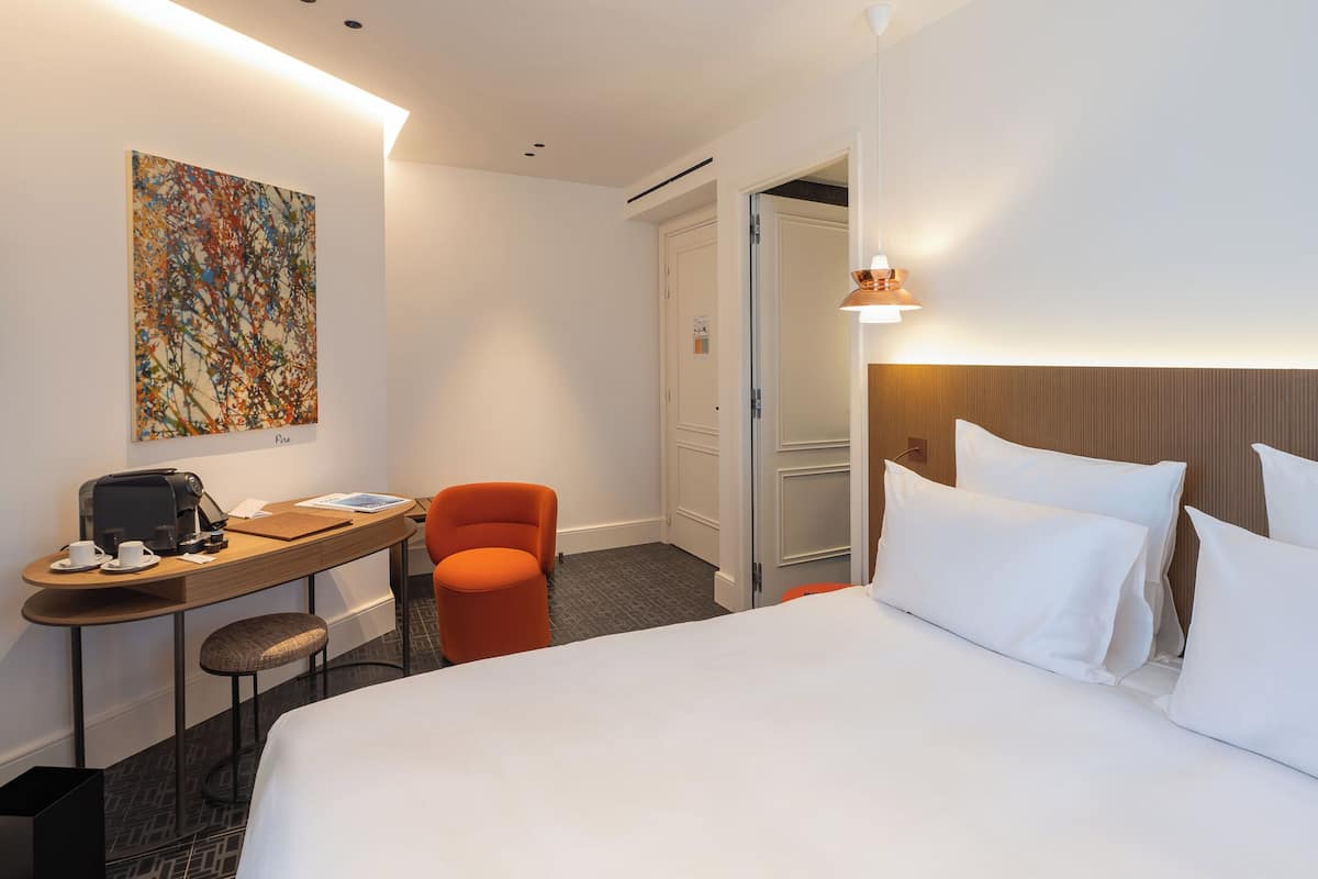 Ein Hotelzimmer mit einem Bett, einem Schreibtisch mit Stuhl, einer Kaffeemaschine und einem Bild an der Wand.