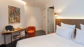 A hotel room with a bed, a desk with a chair, a coffee maker, and a painting on the wall.