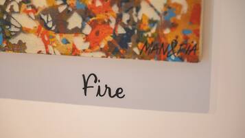 Una pintura abstracta y colorida con la palabra “Fire” y la firma del artista “MAN & RIA” sobre un fondo blanco.