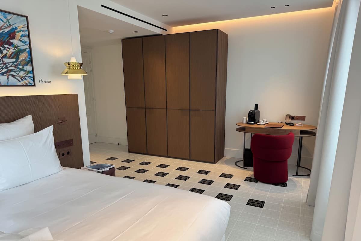 Ein Hotelzimmer mit Bett, Schreibtisch mit Stuhl, Kleiderschrank und einem Bild an der Wand.