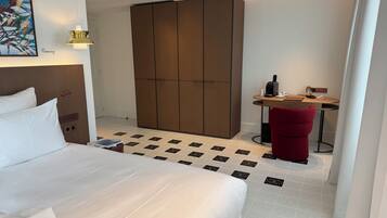 Habitación de hotel con cama, escritorio con silla, armario y un cuadro en la pared.