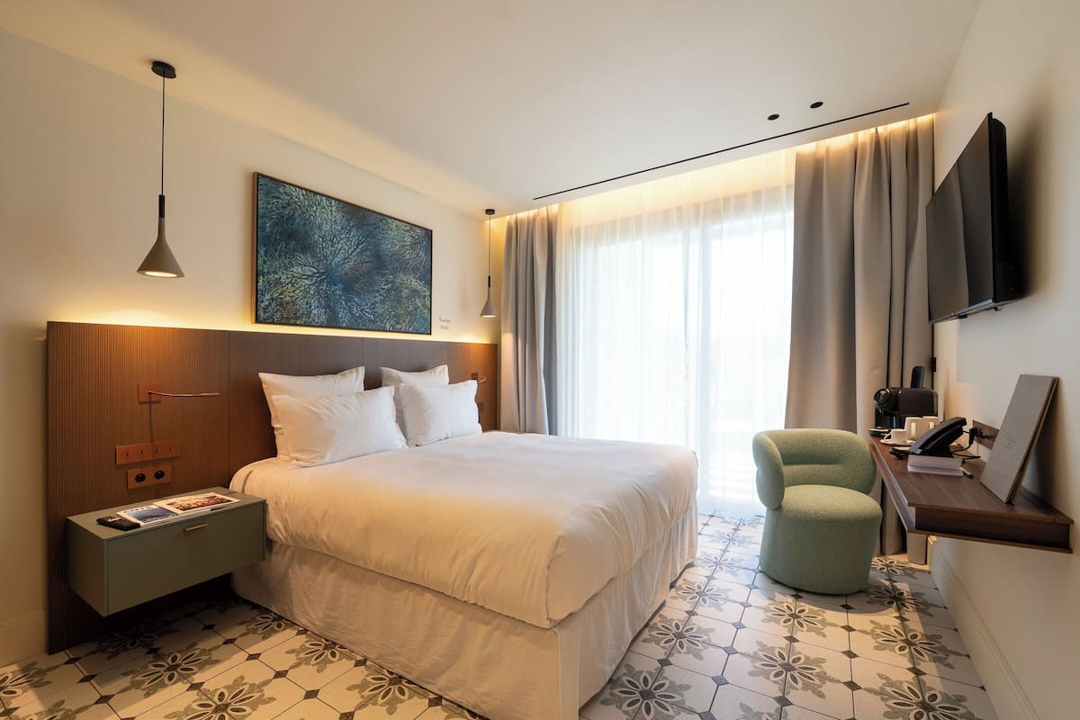 Ein Hotelzimmer mit einem großen Bett, einem Nachttisch, einem Schreibtisch mit Stuhl, einem Flachbildfernseher und einem Bild an der Wand.