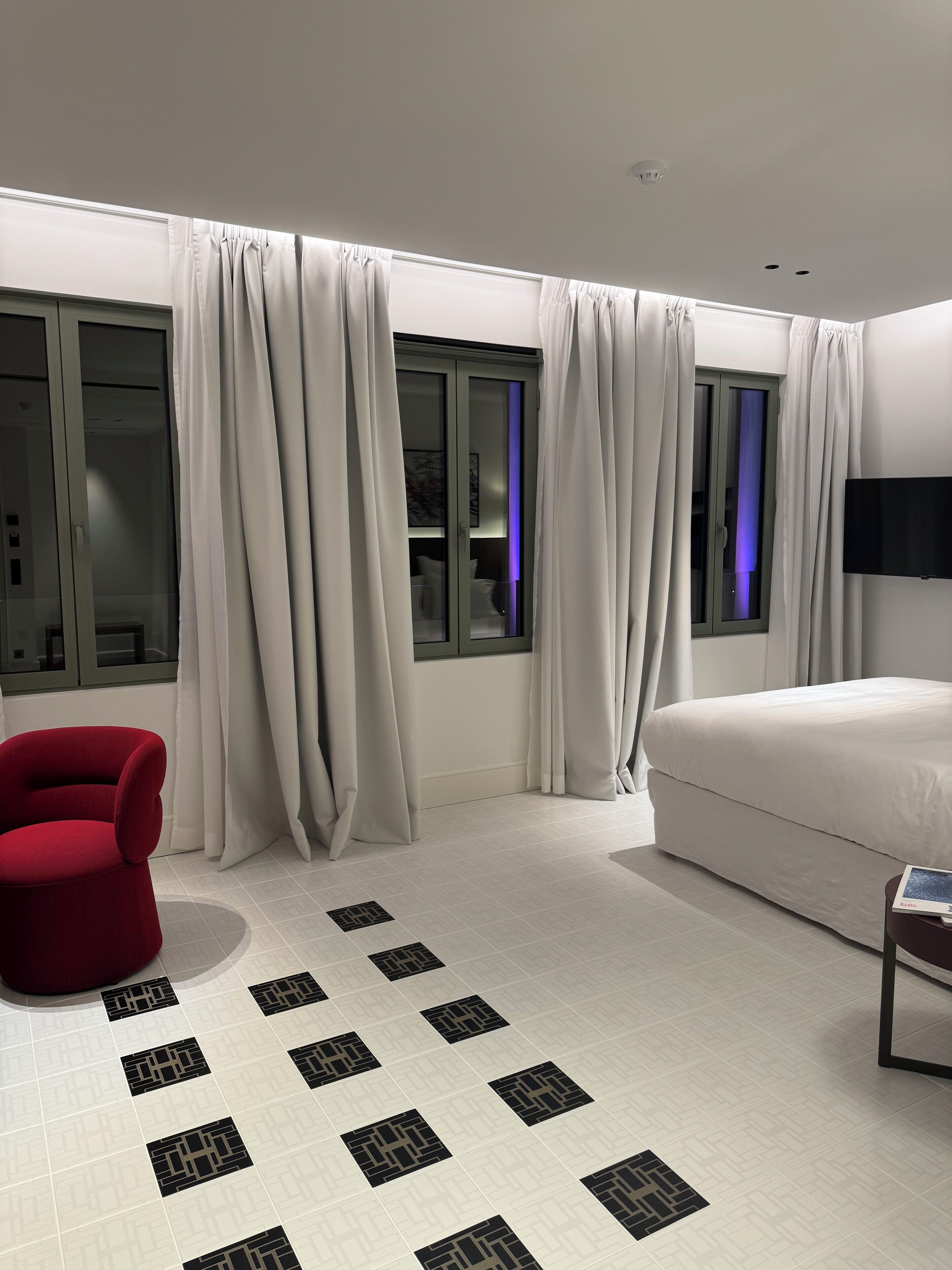 A modern bedroom with a large bed, a red chair, and a TV on the wall.