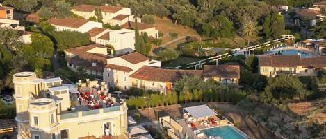 A coastal resort with a swimming pool, multiple buildings, and a view of the sea with boats.