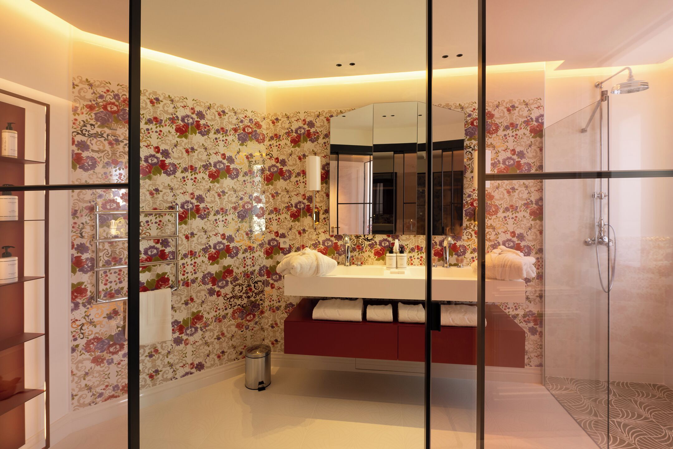 Un baño moderno con papel tapiz floral, una ducha con cerramiento de vidrio y un tocador con espejo.