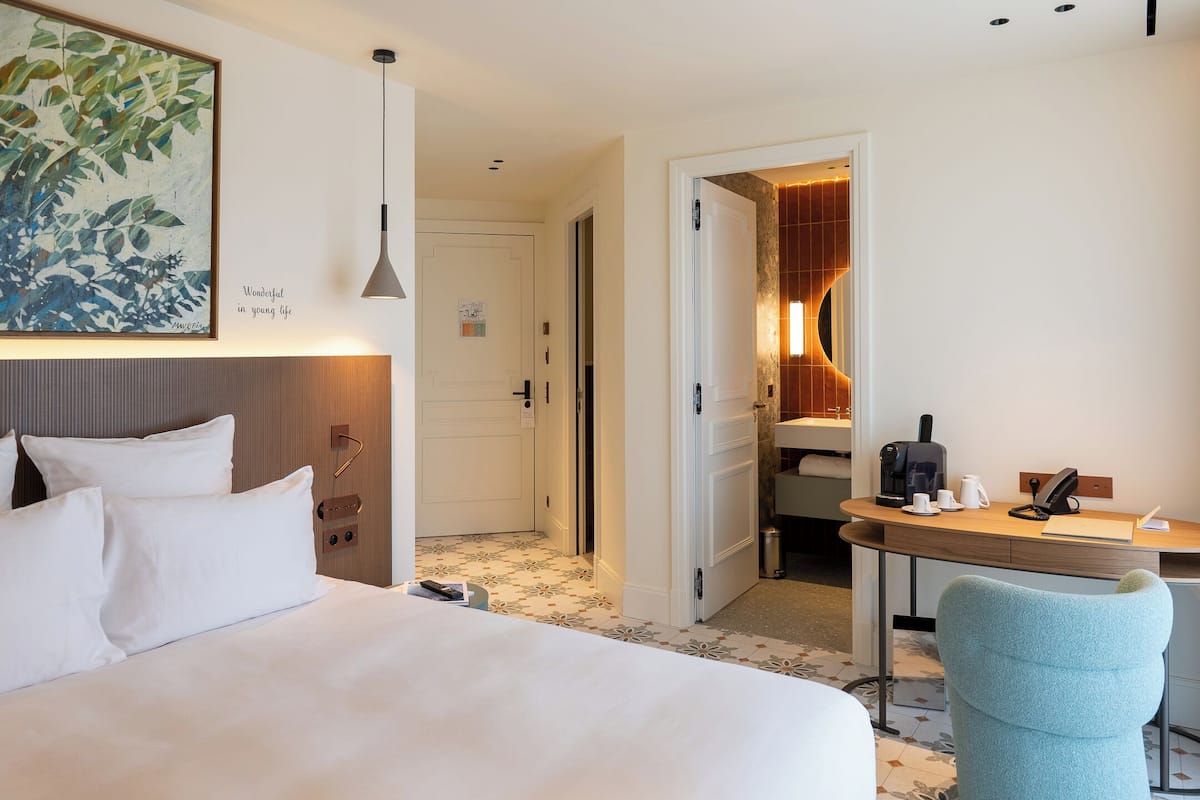 Ein Hotelzimmer mit einem Bett, einem Schreibtisch, einem Stuhl und einem durch eine geöffnete Tür einsehbaren Badezimmer.