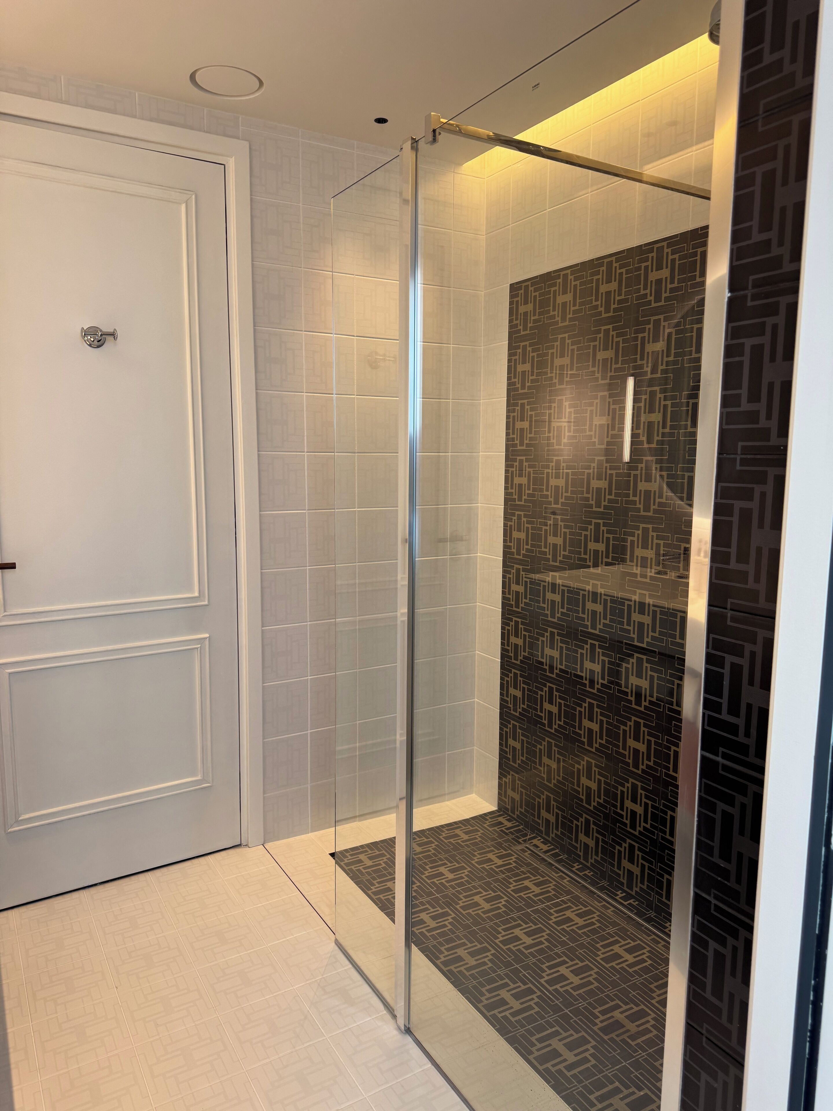 A modern bathroom with a glass shower enclosure, patterned tiles, and a white door.