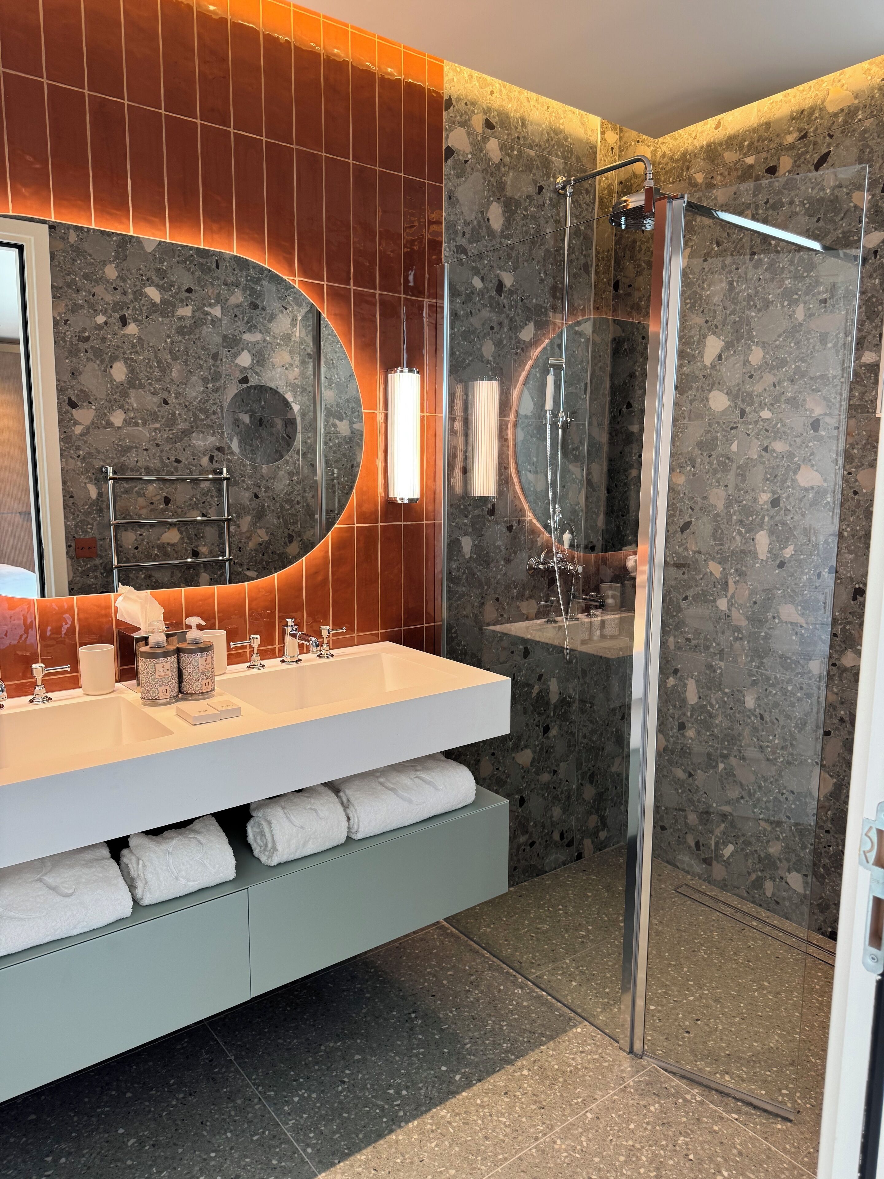 A modern bathroom with a dual sink vanity, a glass-enclosed shower, and a large mirror with a circular frame.