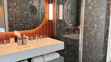 A modern bathroom with a dual sink vanity, a glass-enclosed shower, and a large mirror with a circular frame.