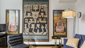 Ett rum med ett stort konstverk inramat, en modern stol, en soffa, en lampa och ett litet bord.
