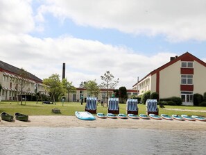 En gårdhave med liggestole og en række små både, omgivet af bygninger med en rød og hvid facade.