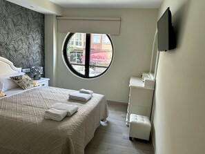 Quarto com uma cama, uma janela redonda, uma TV branca e uma cadeira branca.