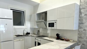 A modern kitchen with white cabinetry, a marble countertop, a built-in oven, a microwave, and a coffee machine.