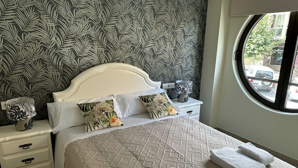 A neatly made bed with a patterned bedspread, two pillows, and a bedside lamp on a nightstand.