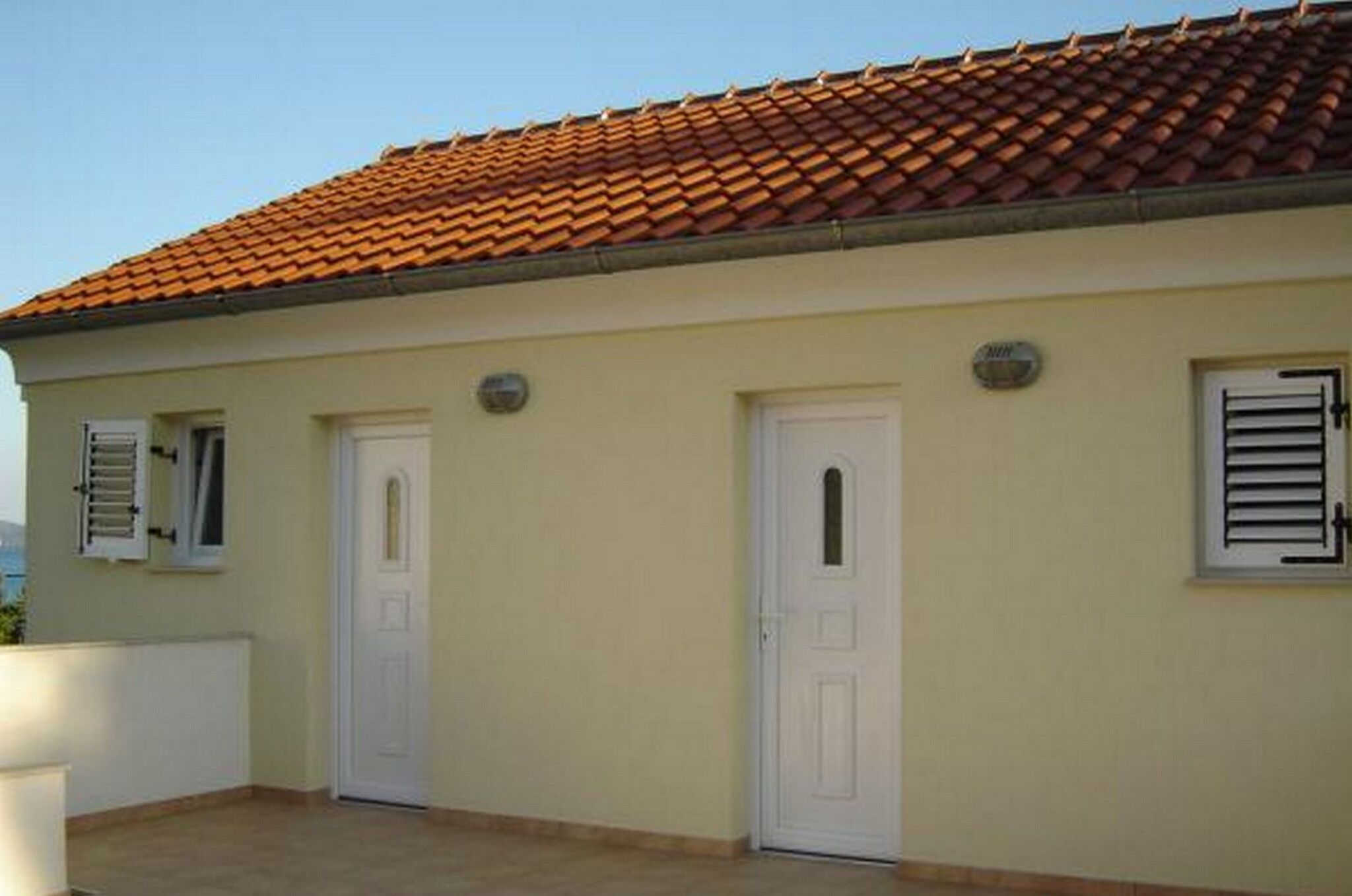 A building with a tiled roof, two white doors, and a small window with shutters.
