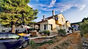 A two-story house with a red roof, a chimney, and a satellite dish. There is a car parked in front and a tree to the left. - Studio Apartments Darija - A2 (Brgulje)