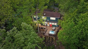Une maison à deux étages, entourée d’une forêt dense, avec une terrasse et un jacuzzi.