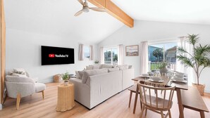 A modern living room with a sofa, a TV mounted on the wall, a dining table set, and a ceiling fan. - Walk to Vilano Beach + Pool + Hot Tub + Pets (St. Augustine)
