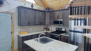 A kitchen with grey cabinets, a stainless steel refrigerator, a microwave, and a gas stove. - Kabino: River Run Cabin on Henry's Fork, Fire Pit, perfect fishing trip! (Ashton)