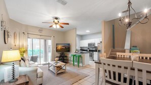 A spacious living area with a sofa, coffee table, and a TV. There is a kitchen with modern appliances and a dining area with a bench.