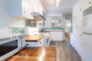 A modern kitchen with white cabinets, a wooden countertop, a built-in oven, and a stainless steel range hood.