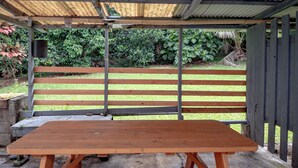 A wooden bench with a metal frame, a concrete table, and a metal roof structure. - Kai Cottage - A Little Piece of Old Hilo (Hilo)