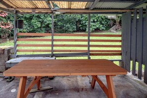 A wooden bench with a metal frame, a concrete table, and a metal roof structure.