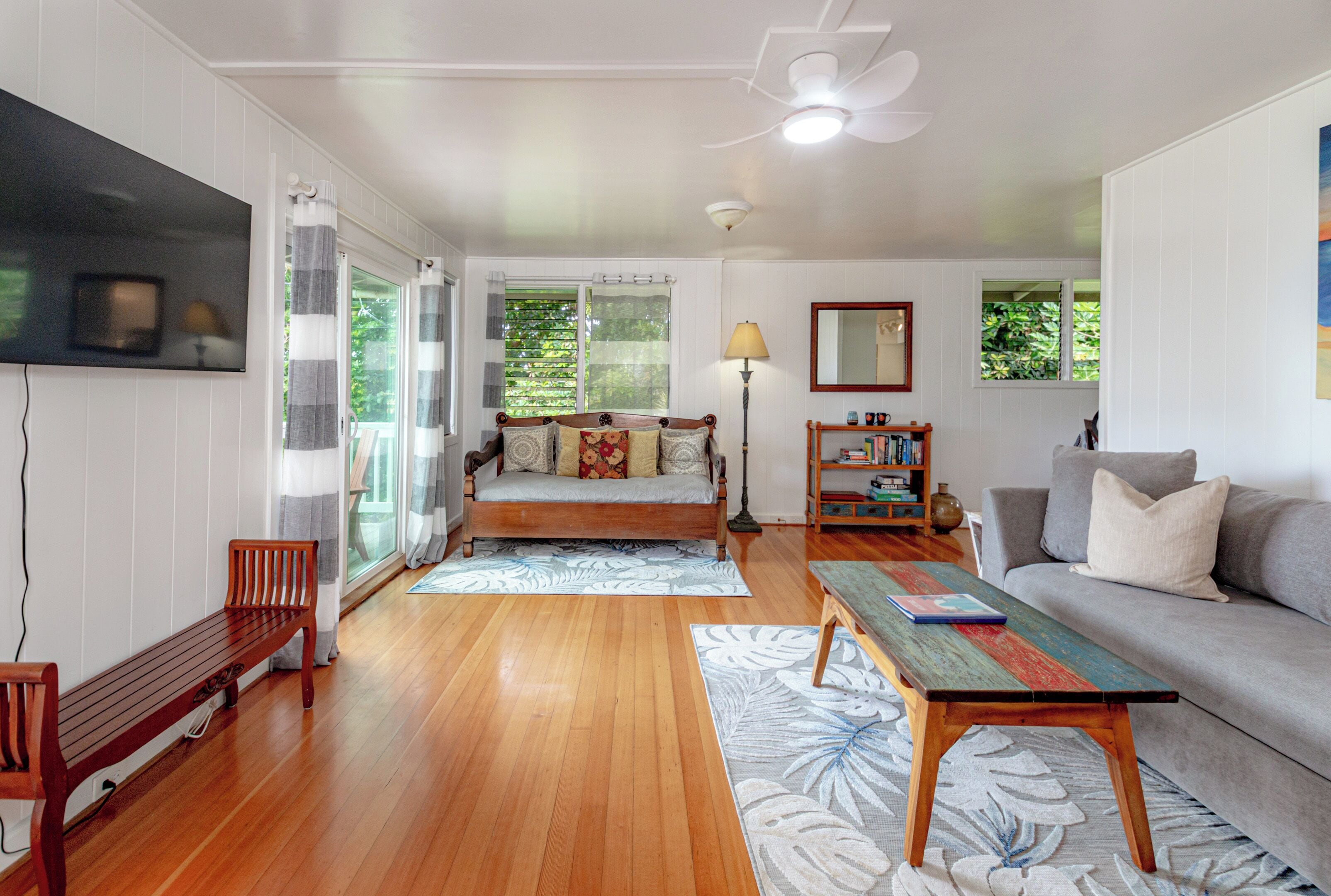 A spacious living room with a wooden floor, a sofa, a coffee table, and a television mounted on the wall.