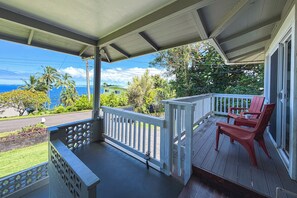 A wooden deck with a railing, a red chair, and a view of the ocean and greenery.