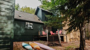 Une maison dotée d’une terrasse et de chaises, entourée d’arbres.