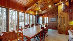 Une cabane en bois avec une grande table à manger, plusieurs chaises et une tête de cerf fixée au mur.