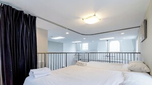 A modern hotel room with a large bed, a mirror, and a view of the city through the window.