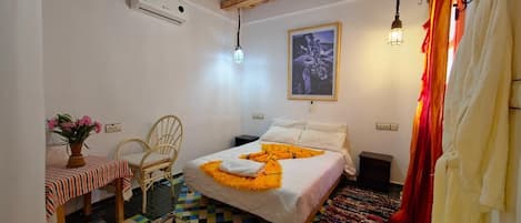 A bedroom with a bed, a chair, a table with a vase, and a hanging light fixture.