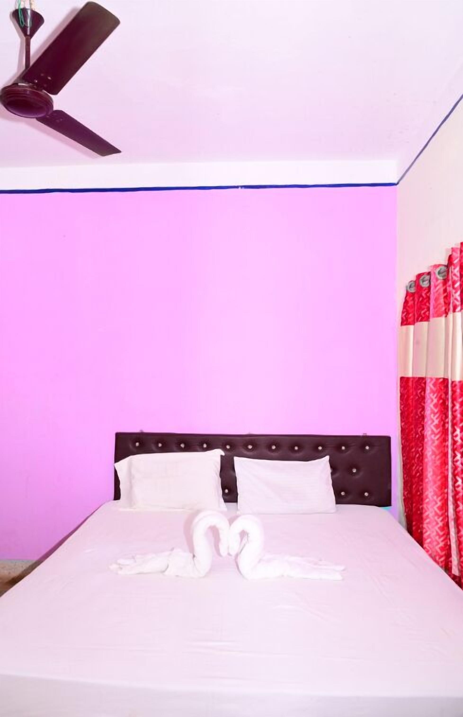A bed with a white bedspread and two swan-shaped pillows, a dark headboard, and a ceiling fan.