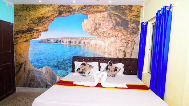 A hotel room with a bed, a mural of a coastal cliff, and blue curtains. - DhamStay Hotel JK Inn Near SeaBeach Puri (Puri)