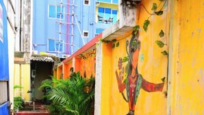 A narrow alleyway with a yellow wall featuring a mural of a deity, potted plants, and a blue building in the background. - DhamStay Hotel JK Inn Near SeaBeach Puri (Puri)