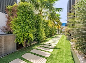 A well-maintained garden with a stone pathway, lush greenery, and a modern building in the background.