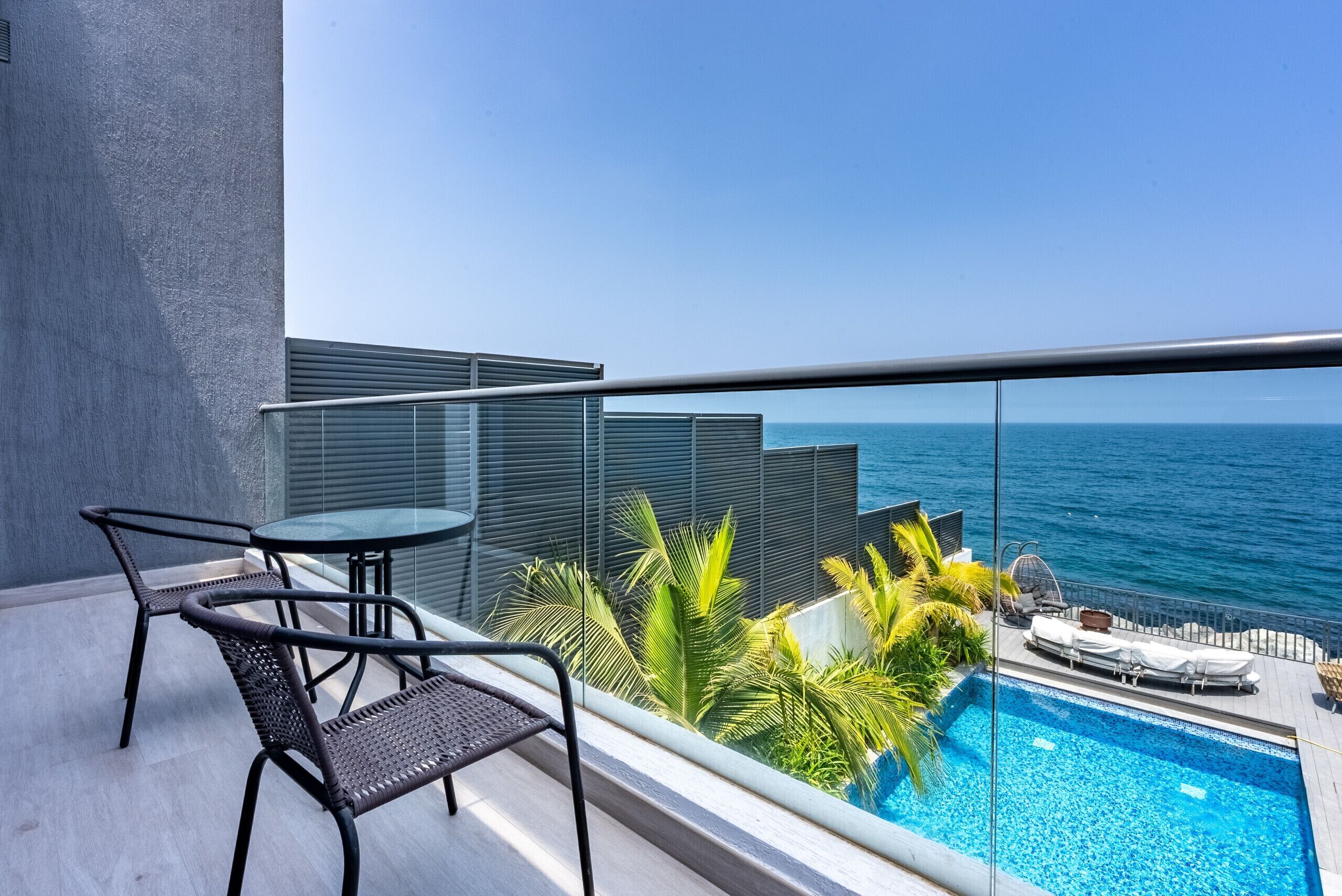 Een balkon met een zwembad, stoelen en uitzicht op zee.