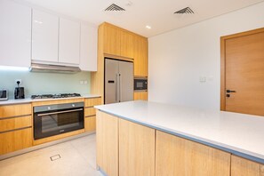 A modern kitchen with wooden cabinets, a stainless steel refrigerator, an oven, and a microwave.