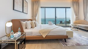 A modern hotel room with a large bed, a glass table with a bottle, a chair, and a view of the sea through large windows. - Exclusive 4BR Villa, Lush Garden & Private Pool Facing Panoramic Sea Views (Fujairah)