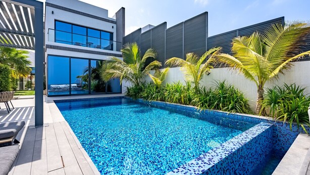 A modern outdoor swimming pool with clear blue water, surrounded by a patio area with seating and plants. - Exclusive 4BR Villa, Lush Garden & Private Pool Facing Panoramic Sea Views (Fujairah)