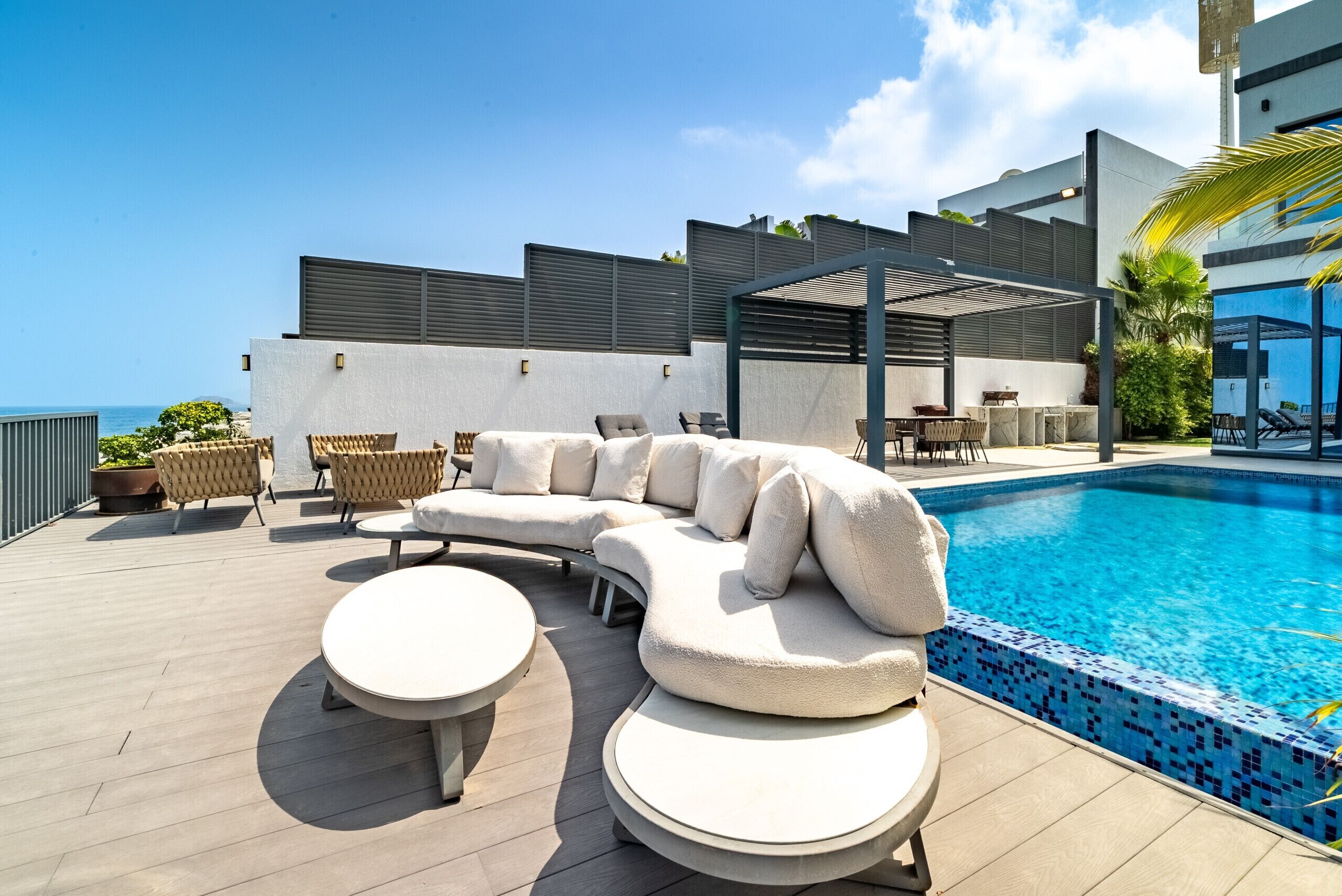 A poolside area with a sectional sofa, two round tables, and a pergola structure.