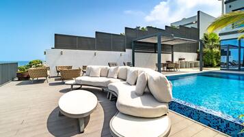 A poolside area with a sectional sofa, two round tables, and a pergola structure.